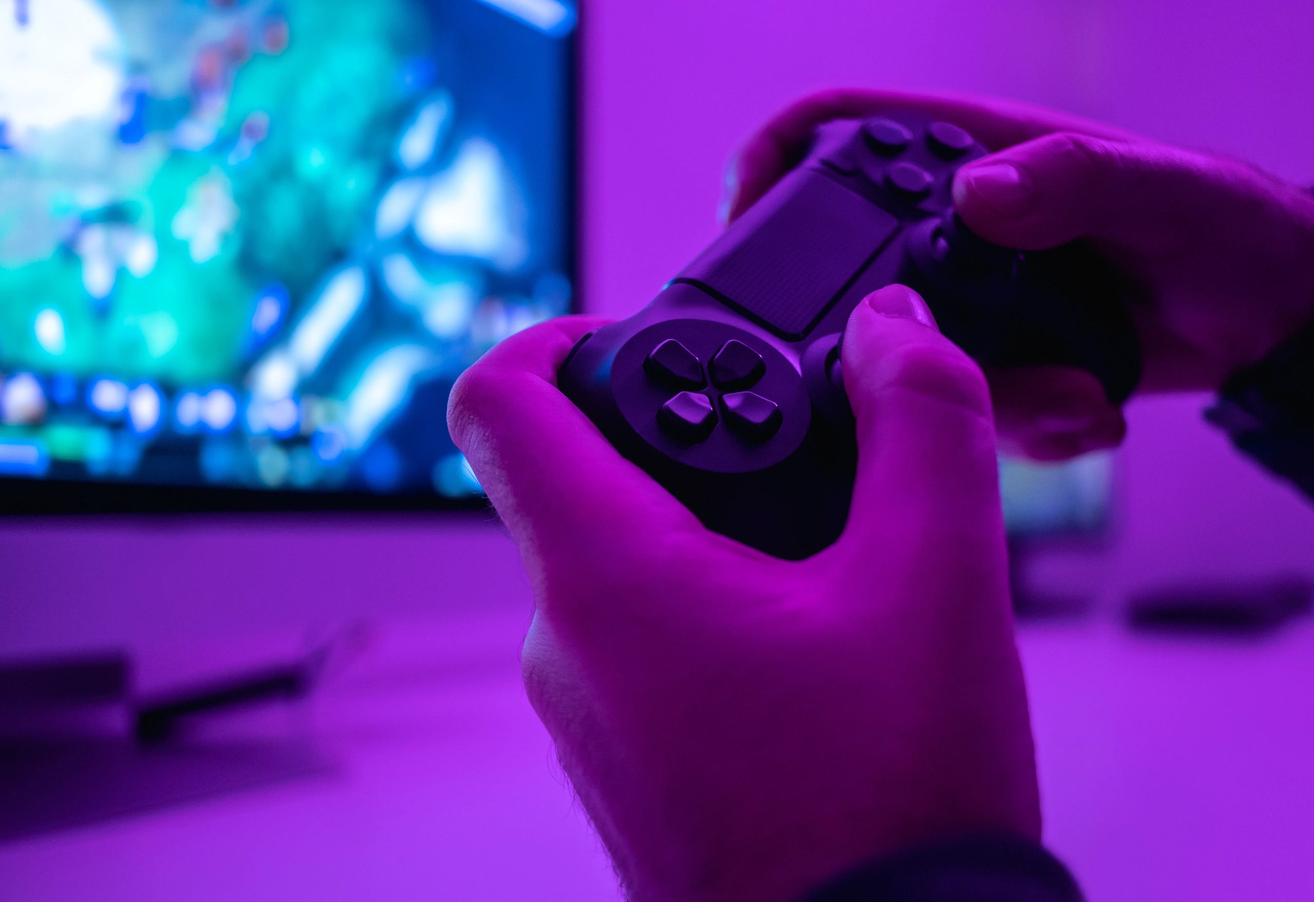 Hands holding a gaming controller with a vibrant blue and purple background.