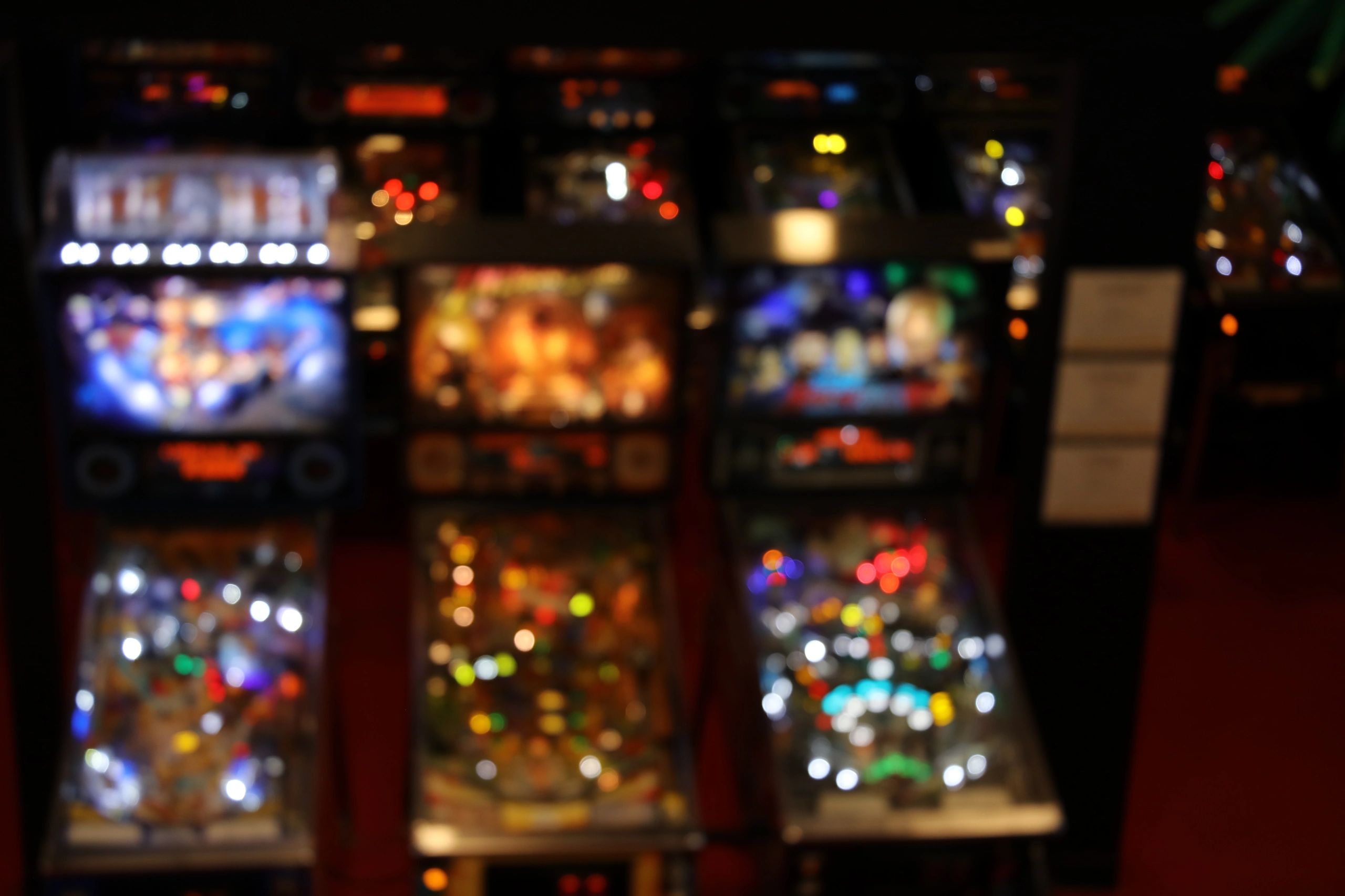 Blurred image of illuminated pinball machines in a dim arcade.